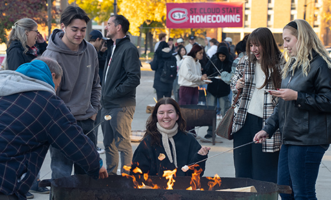 A group of #OurSCSU community members sit around a campfire in Husky Plaza during Homecoming