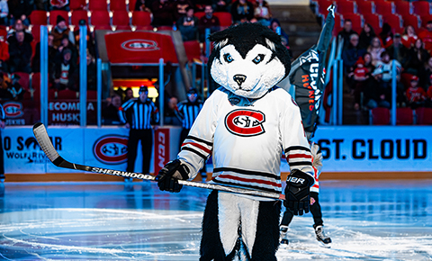 SCSU mascot Blizzard stands on the ice with a hockey stick