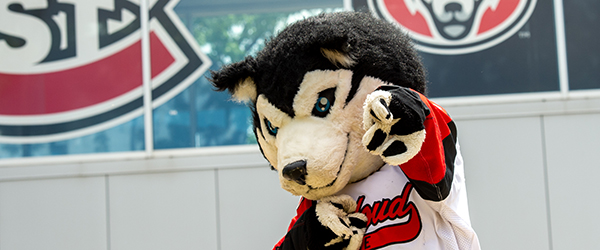 Blizzard the Husky mascot waving with Atwood Memorial Center in the background