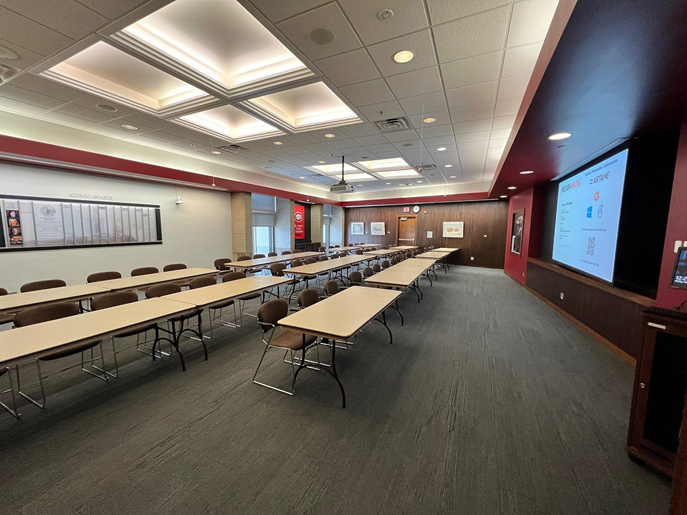 Interior of the Alumni Room at Atwood Memorial Center showing a mid-size meeting space with tables, chairs, and built-in technology for presentations