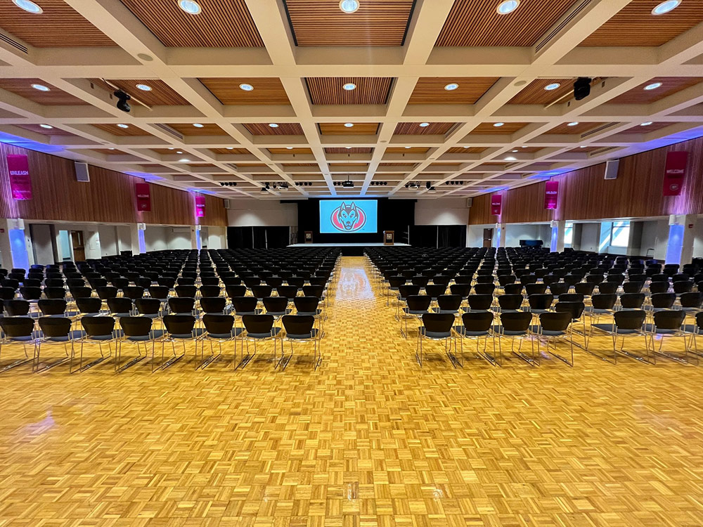 Interior of the Atwood Memorial Center Ballroom showing an open aisle leading toward the stage with rows of chairs on both sides