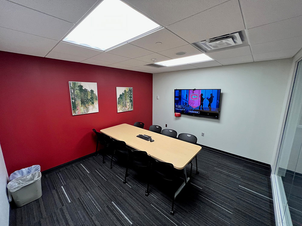 Interior of the Blizzard Room at Atwood Memorial Center showing a table with chairs, art on a red accent wall, and a large computer monitor mounted on a white wall