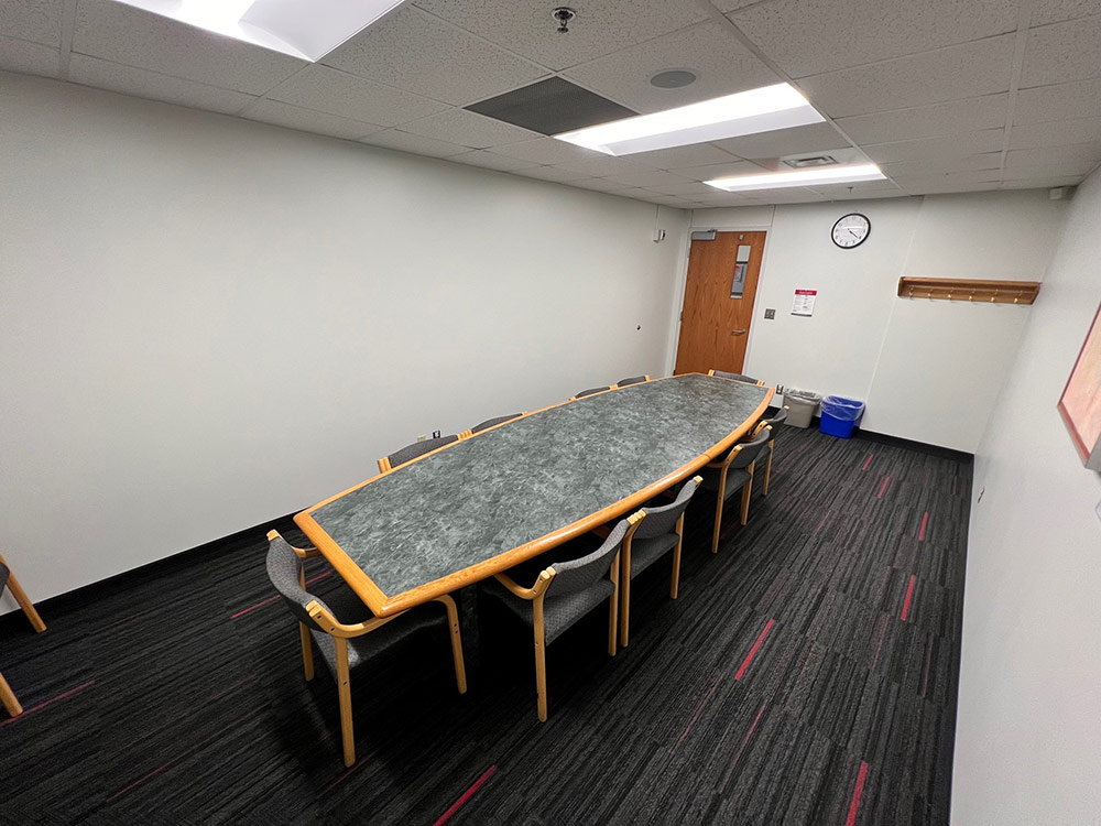Interior of the Iris Room at Atwood Memorial Center viewed from the opposite angle, showing the narrow table with chairs and a wall clock