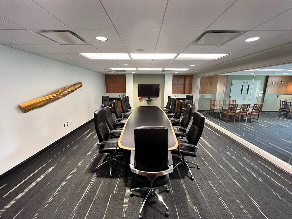 Interior of the Monarch Room in Atwood Memorial Center showing a long conference table with multiple black leather chairs around it, modern lighting, and a wall sculpture on the left