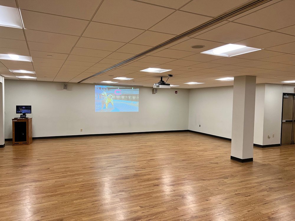 Interior view of Atwood Memorial Center rehearsal room showing hardwood floor, a desktop screen on the wall, and AV equipment