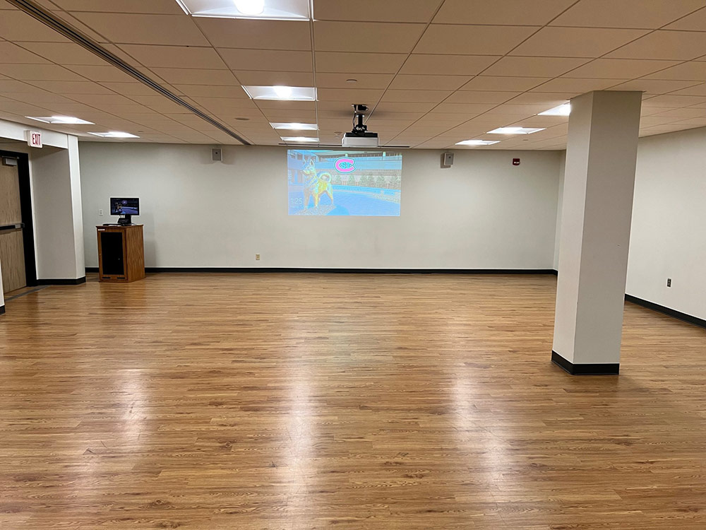 Wide interior of Atwood Memorial Center rehearsal room with hardwood floor and a desktop screen on the wall