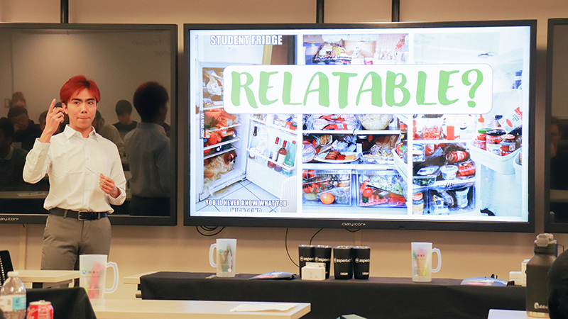 A student stands beside a large presentation screen while holding a handheld presentation clicker