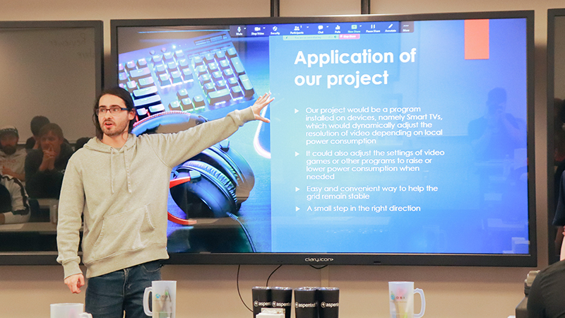 A student stands beside a large presentation screen with an arm extended toward the screen