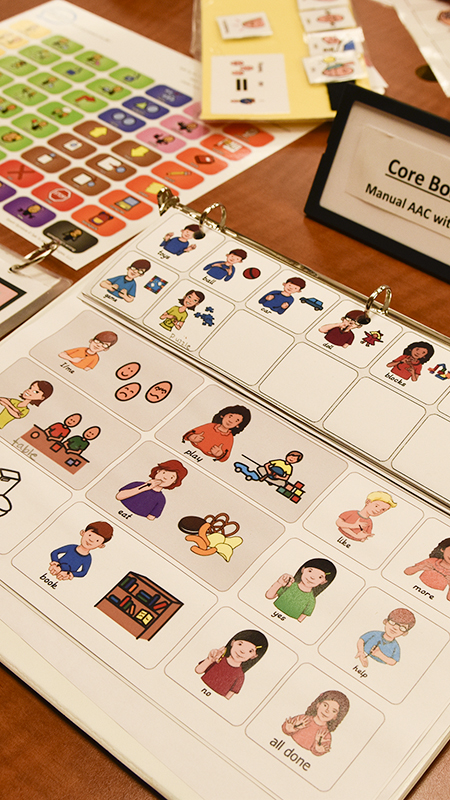 An open communication binder displays illustrated picture symbols arranged in a grid on a tabletop