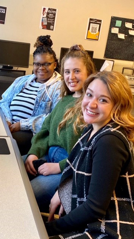 Three students sit together for a group photo near computers