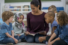 An adult reads a book to several children in a library setting