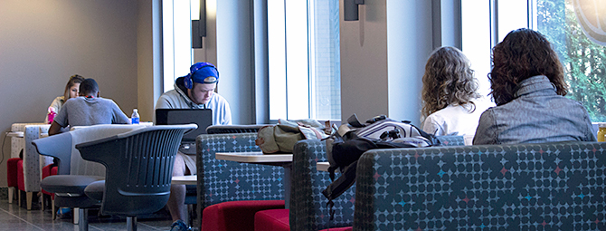 Several students study together in a lounge‑style room, seated near large windows that let in natural light