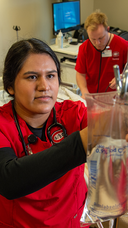 Nursing student adjusting an IV fluid bag with two other students in the background