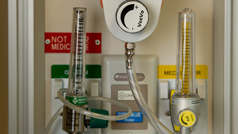 Close-up of a medical gas panel showing two vertical flow meters with clear tubes, connected tubing, and a central control knob