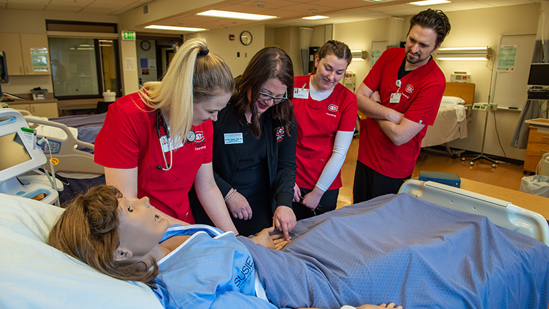 Nursing instructor assisting students during a patient care simulation