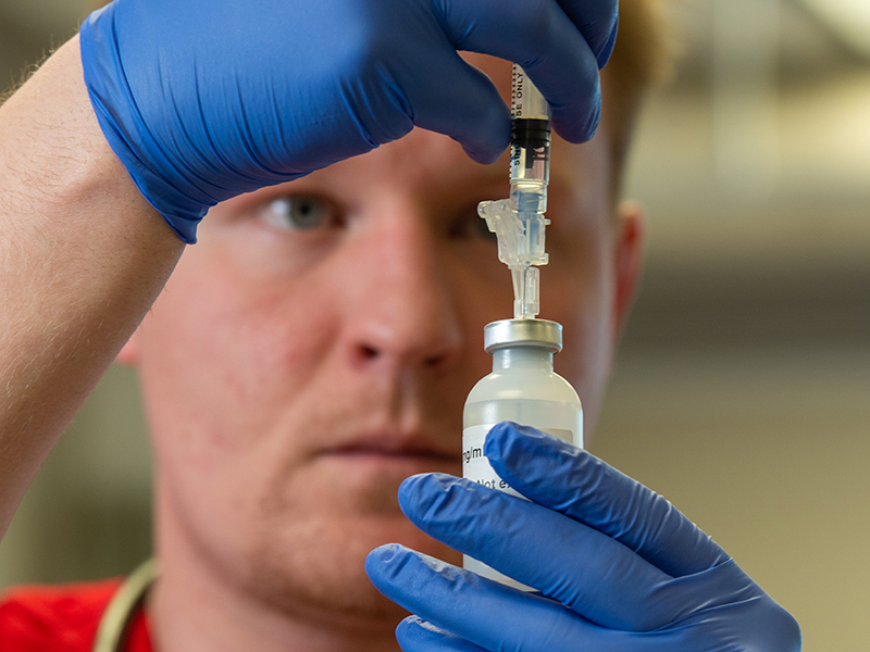Person wearing medical gloves carefully filling a syringe