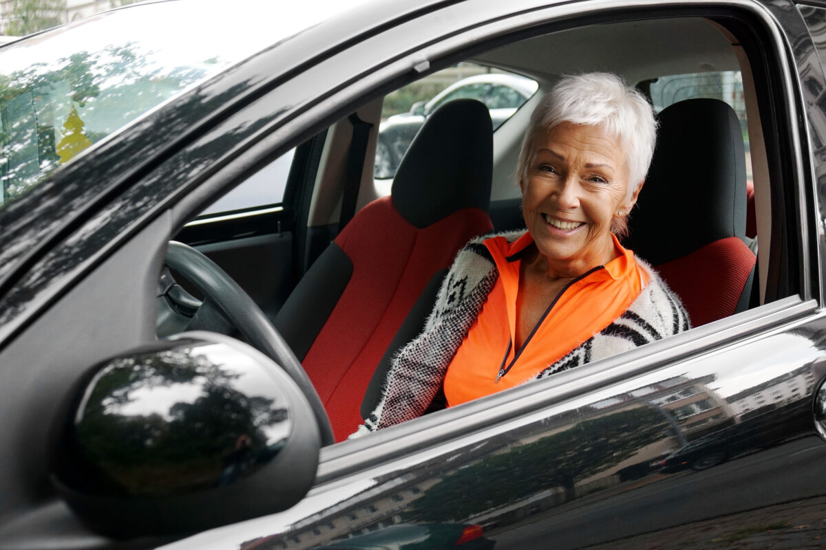 Person seated in a parked car with the driver-side window rolled down, looking outward through the open window